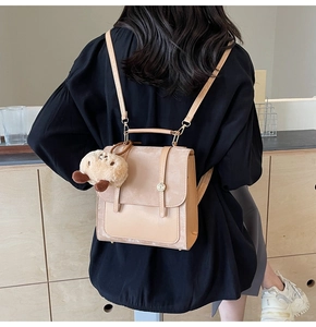 Detail eines beigen Retro-Rucksacks mit Plüschanhänger, am Modell getragen