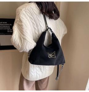 Fashionable black suede shoulder bag with gold butterfly embroidery on white sweater model
