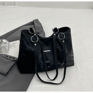 Close-up of black tote bag with wrinkled texture and silver hardware on white fabric