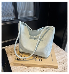 Gros plan d'un sac seau bleu menthe avec nœud et texture plissée posé sur un livre