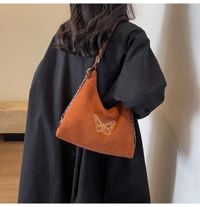 Detailed view of butterfly embroidery and chain strap on orange suede shoulder bag