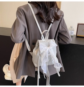 Detail of silver metallic backpack featuring a white lace bow and drawstring closure