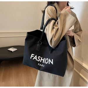 Close-up of black canvas tote bag with Fashion Paris print worn on shoulder