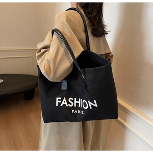 Detail of black canvas tote bag with white Fashion Paris text and leather handles