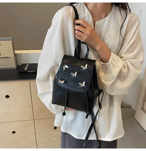 Close-up of a mini black PU leather backpack with silver butterfly accents on the model