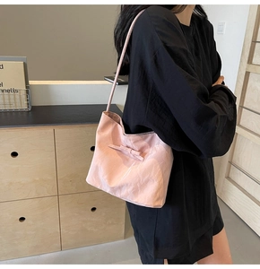 Sac seau plissé rose avec nœud, porté à l'épaule dans un intérieur moderne