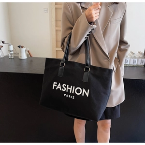 Detail of a black canvas tote bag with white lettering held by a model in a café