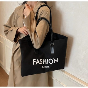 Large black canvas tote bag with white letter print styled with an elegant trench coat