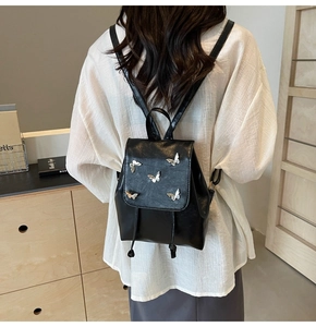 Detail of mini black leather backpack featuring silver butterfly accents and drawstring