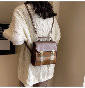 Detail of vintage brown plaid backpack with gold metal buckles on white cable knit sweater