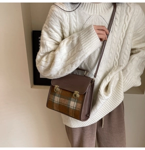 Brown vintage leather crossbody bag with plaid fabric trim worn by a model in a cozy sweater