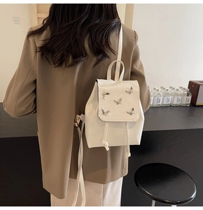 Rear view of model wearing a white PU leather mini backpack with silver butterfly accents