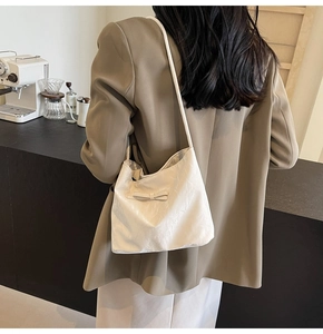 Gros plan du sac seau à nœud crème porté par un mannequin dans un café