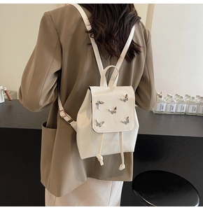 Detailed back view of a white leather mini backpack with silver butterfly accents on a model
