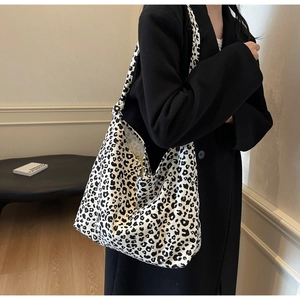 Close-up of leopard print canvas hobo bag worn with a black coat in a minimalist setting