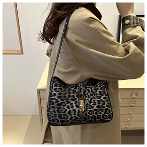 Detail view of a leopard print underarm bag with gold clasp worn by a model