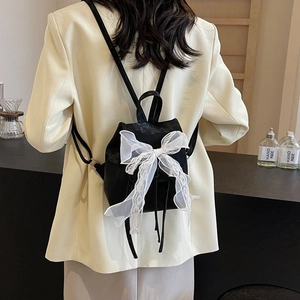 Black ballet-style backpack with white lace bow and drawstring in a cozy setting