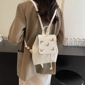 Mini white leather backpack with silver butterfly accents shown on a female model