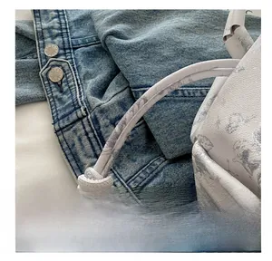 Close-up of floral print handbag with textured handle on blue denim jacket
