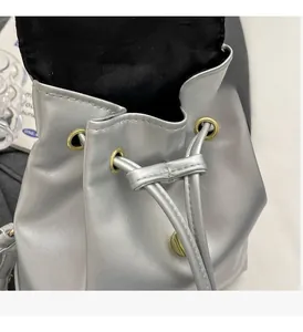 Detail of silver metallic drawstring bucket bag featuring premium gold hardware accents