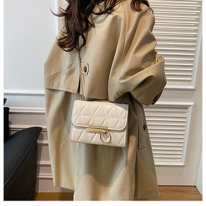 Detailed view of white quilted crossbody bag with gold hardware worn over a khaki coat
