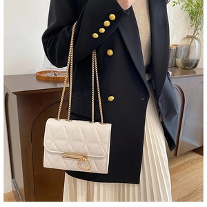 Detail of cream white quilted chain bag with gold ring lock on a stylish outfit