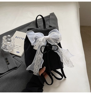 Détail d'un sac à dos en daim noir avec un grand nœud en dentelle blanche et cordon