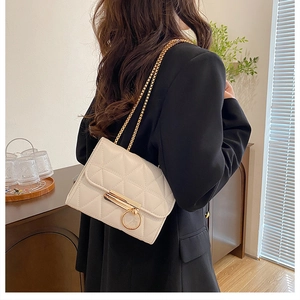 Quilted beige shoulder bag with gold chain strap shown on black blazer in a cozy setting