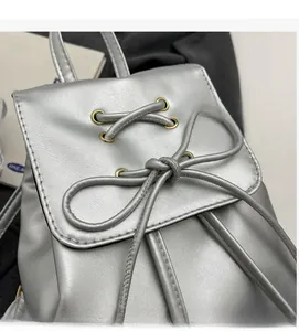 Detailed close-up of silver metallic leather backpack featuring decorative lace-up bow and eyelets