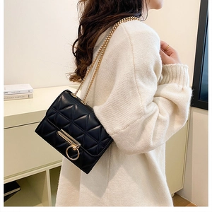 Close-up of black quilted shoulder bag with gold chain strap and metal ring lock