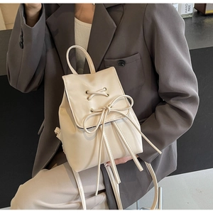 Close-up of cream mini backpack featuring a decorative lace-up bow and long tassel detail