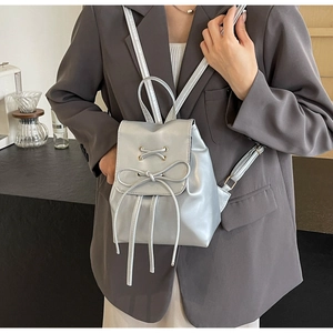 Détail d'un mini sac à dos argenté avec nœud en ruban et lanières croisées en similicuir
