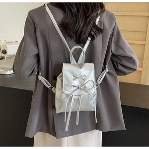 Chic silver mini backpack with bow detail worn by model over a grey blazer