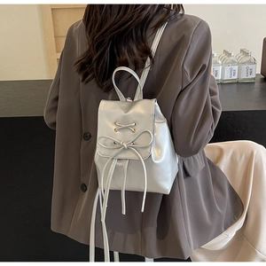 Detail of silver metallic mini backpack with bow ties shown on a model in a cafe setting