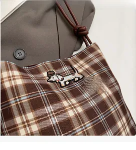Detail of plaid fabric shoulder bag featuring embroidered dachshund and leather rope strap