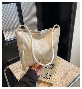 Detail of white jacquard bucket bag with traditional pattern and elegant tassel charm
