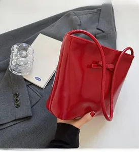 Detail of red patent leather shoulder bag with chic bow on gray suit and book