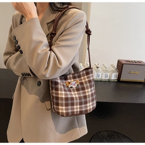 Detailed close-up of brown plaid bucket bag with cartoon embroidery and knotted leather strap