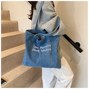 Detail of blue denim tote bag with Less Mondays More Sundays white embroidery text