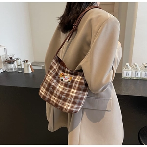 Detail of a brown plaid shoulder bag featuring a cute bear patch and rope strap design
