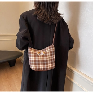 Detail of a brown plaid shoulder bag with a bear embroidery patch on a model
