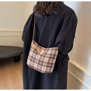 Detail of brown plaid crossbody bag featuring a cute cartoon bear embroidery patch