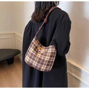 Detail of a brown plaid underarm bag featuring a cute bear patch and slim leather strap