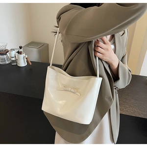 Detail of cream white leather underarm bag with a decorative bow on olive blazer