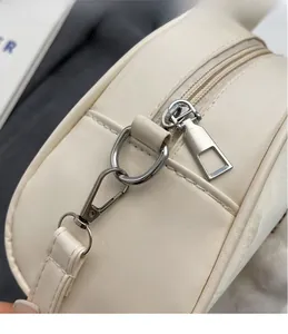 Close-up of silver hardware hooks and zipper detail on cream crossbody bag