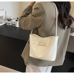 Sac à épaule blanc brillant avec nœud porté par un mannequin dans un cadre de café