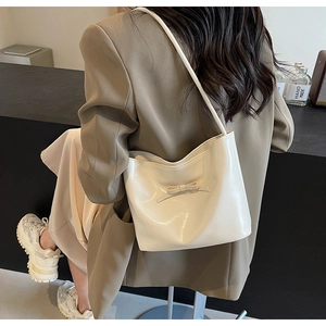 Sac seau chic en cuir verni beige avec nœud porté comme sac à bandoulière sous le bras