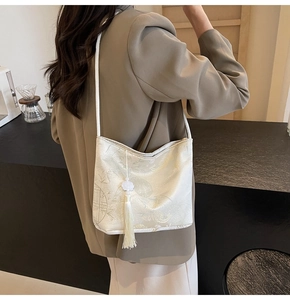 Detail of cream-colored shoulder bag with traditional Chinese jacquard and tassel charm
