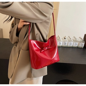 Détail d'un sac hobo en cuir verni rouge avec nœud décoratif porté à l'épaule