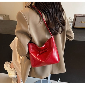 Détail d'un sac à bandoulière rouge brillant avec nœud, porté avec un tailleur kaki